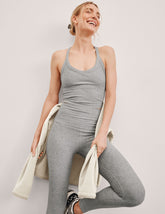 model wearing a gray v-neck cropped tank with a high racerback and gray high-waisted midi length leggings holding a white jacket on a light background.